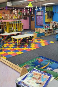 Picture of the Lions classroom which contains some small tables, small chairs, and play equipment.