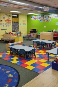 Picture of the Whales classroom which contains some small tables, small chairs, and play equipment.